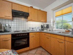 A kitchen with wooden cabinets, a stove, a toaster, and a window with blinds. - Stortebekerstrasse 9 - Apartment 5 (Zingst)