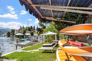 Um cenário à beira de um lago com área coberta, piscina e canoas.
