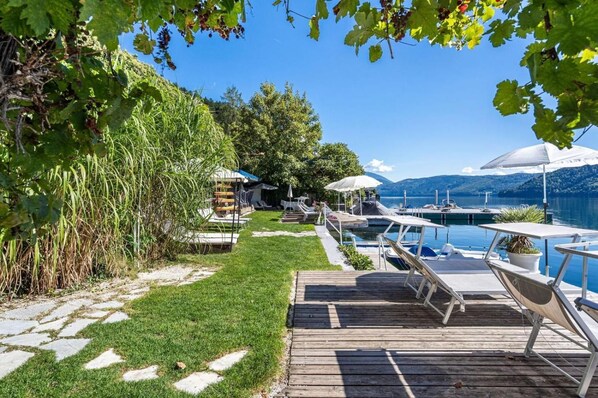 A lakeside property with a wooden deck, lounge chairs, and a swimming pool. - Hotel Nikolasch (Millstatt)