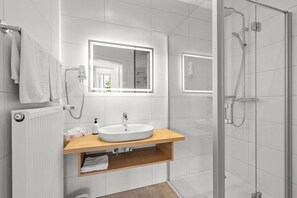 A modern bathroom with a white sink, mirror, and shower. - Hotel Nikolasch (Millstatt)