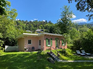 A pink house with green shutters, a white picket fence, and a small porch with chairs. - Hotel Nikolasch (Millstatt)