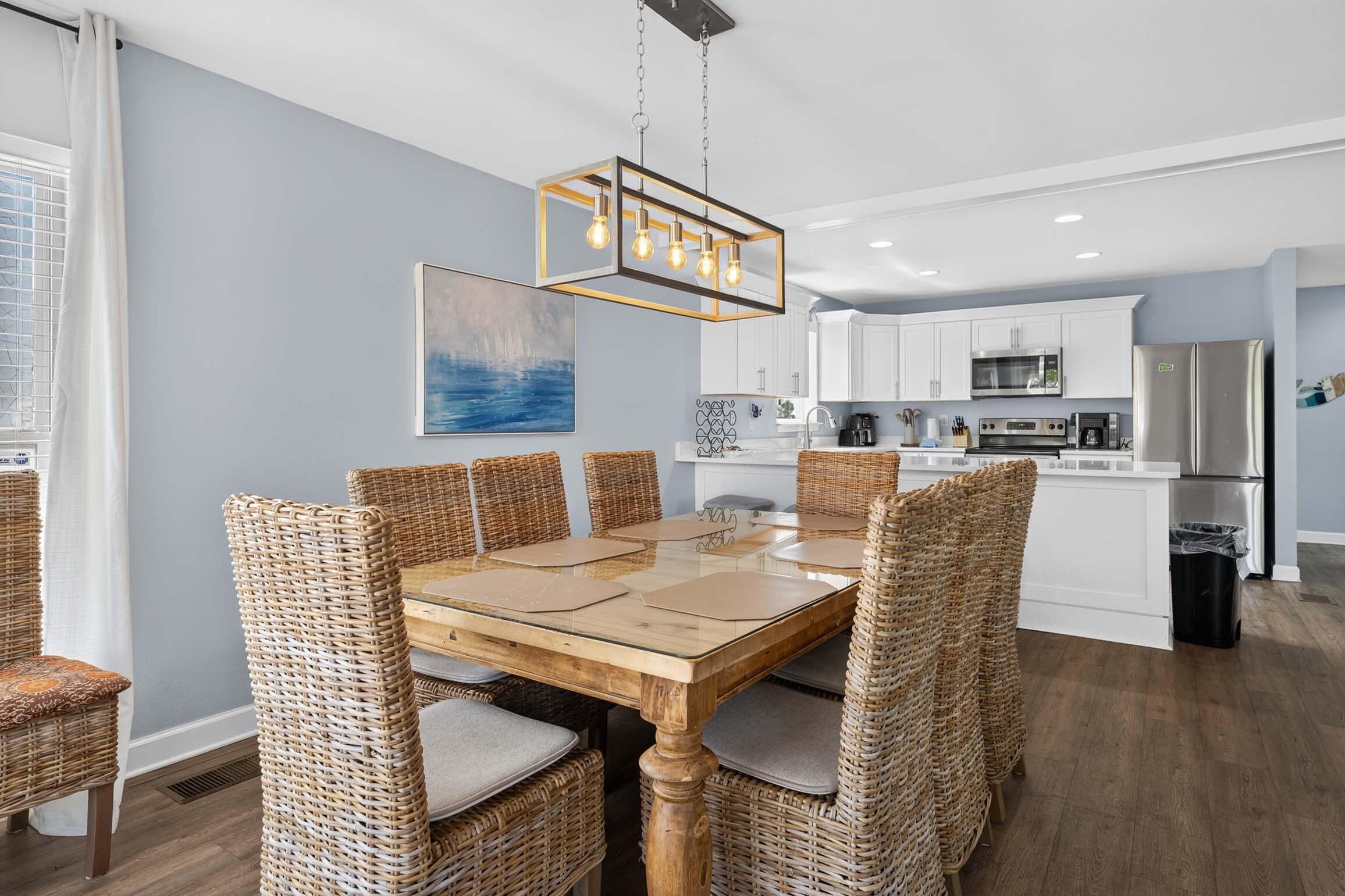 A modern kitchen with white cabinets, stainless steel appliances, and a dining area with a wooden table and wicker chairs.