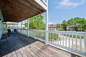 A wooden deck with a covered area, white railings, and a view of surrounding buildings and trees. - The Great Escape (Gulf Shores)