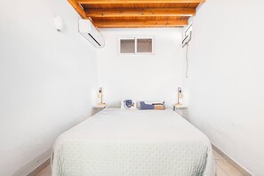 A bedroom with a bed, two bedside lamps, a window, and an air conditioning unit. - Charming 2-Bedroom Apartment with Pool, Terrace, and Air Conditioning (Las Palmas)