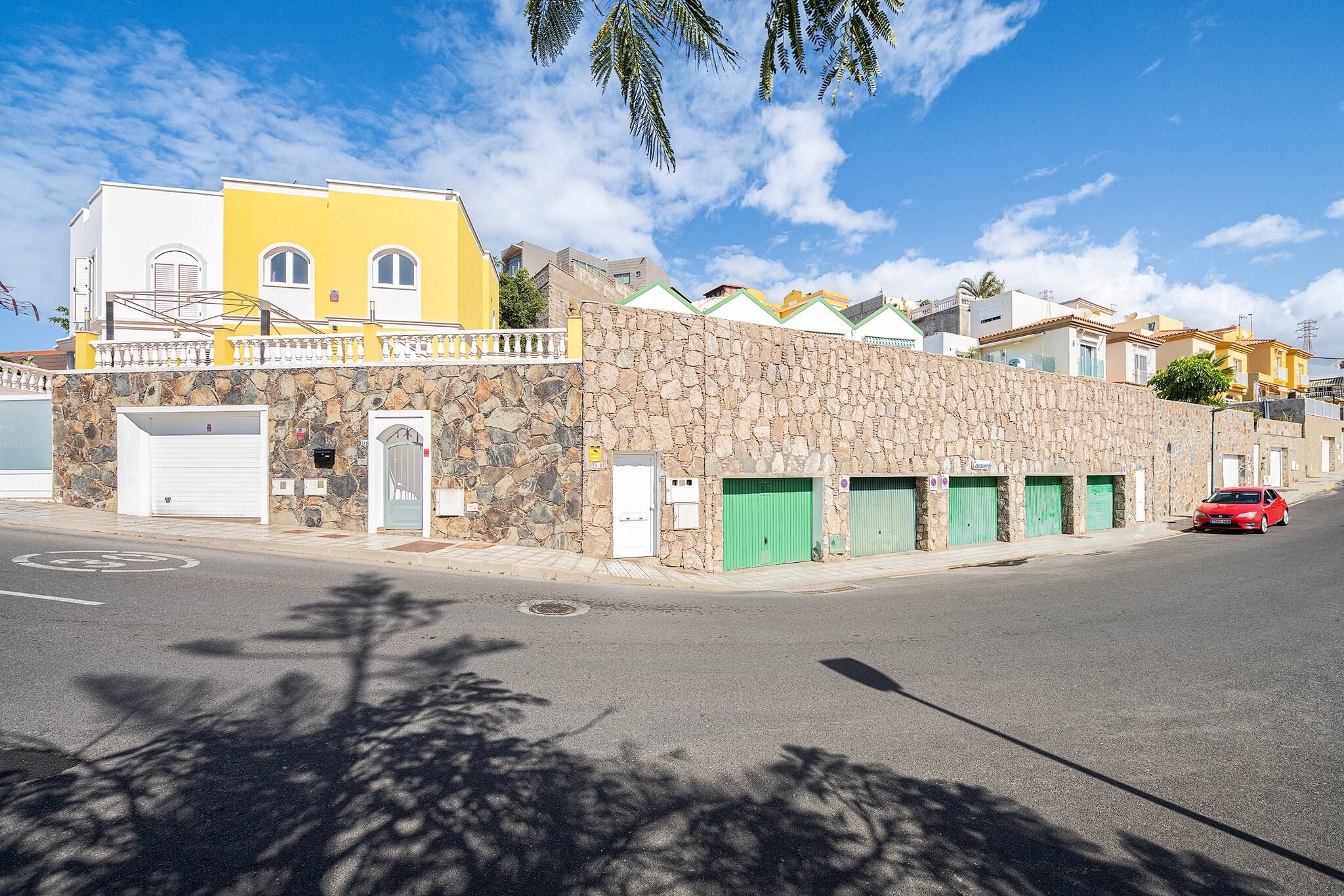Une vue de rue avec un immeuble jaune, un mur de pierre et une voiture rouge garée sur le bord.