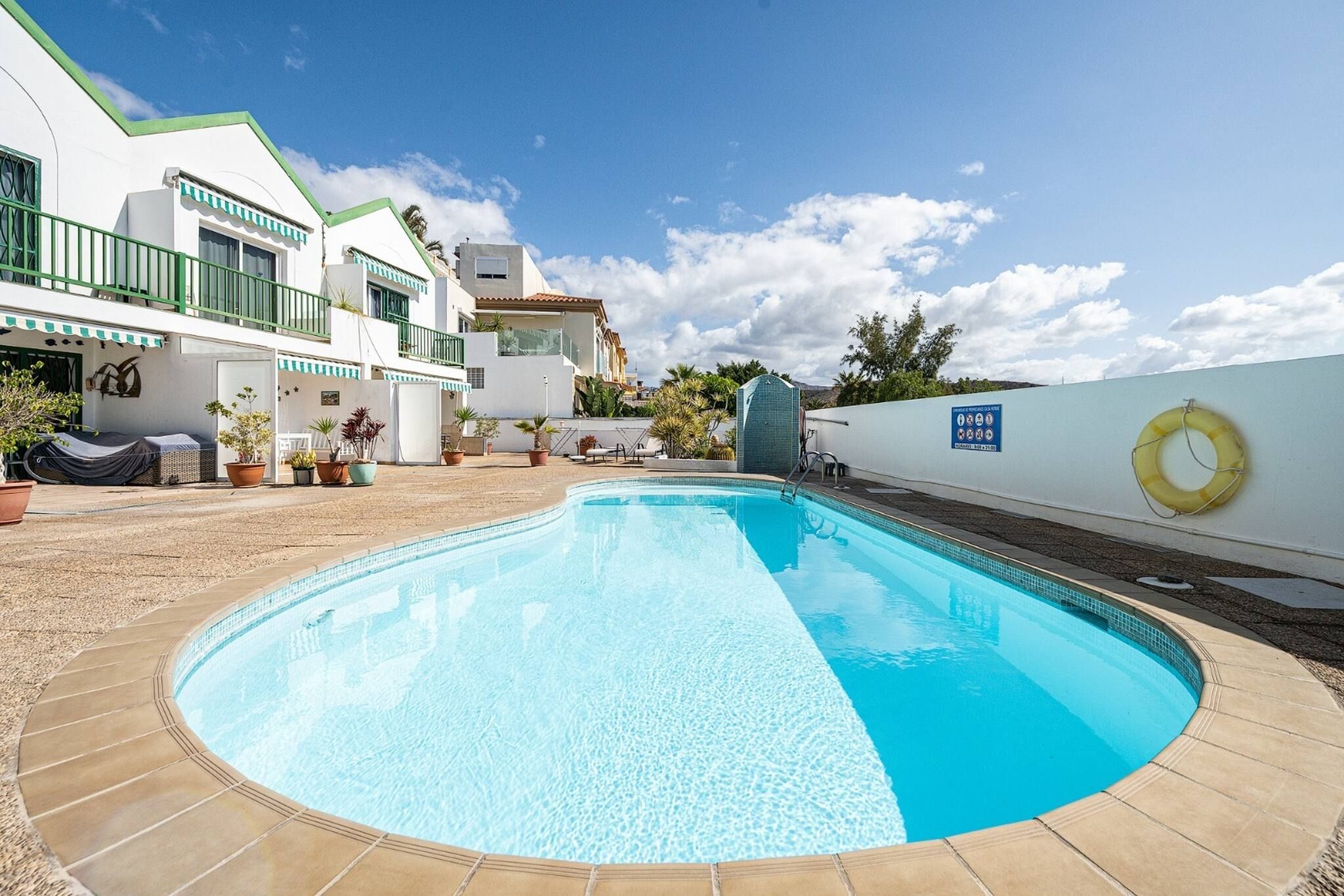 Une piscine dont le bord est revêtu de carreaux, entourée d’une terrasse agrémentée de plantes en pot et de mobilier d’extérieur.