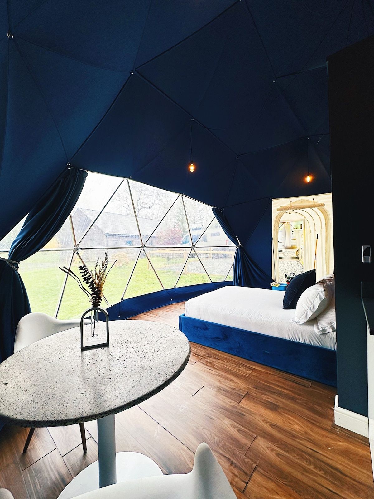 A tented accommodation with a bed, a table, and a view of the outdoors.