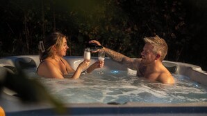 Two people in a hot tub with bubbles, holding drinks. - Luxury Igloo Dome with Hot Tub (Redberth)