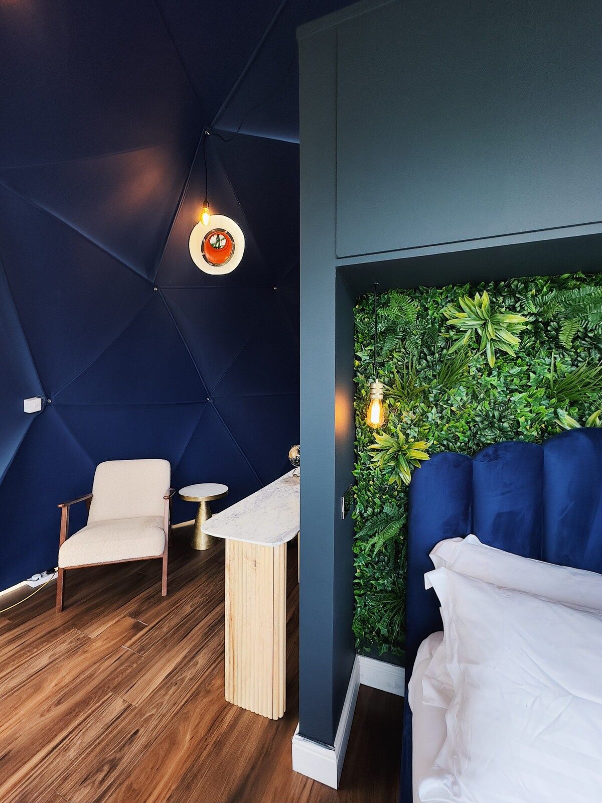A room with a geometric ceiling design, a wall-mounted green plant wall, a white sofa, and a wooden floor.