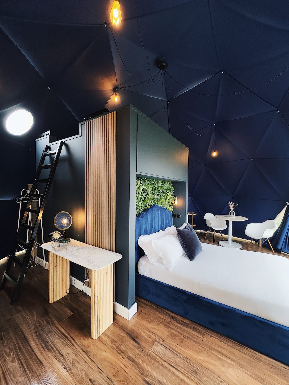 A modern bedroom with a bed, bedside table, lamp, and a small desk with a globe.