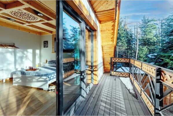 Interior de madera con una cama y un balcón con vistas a un bosque.