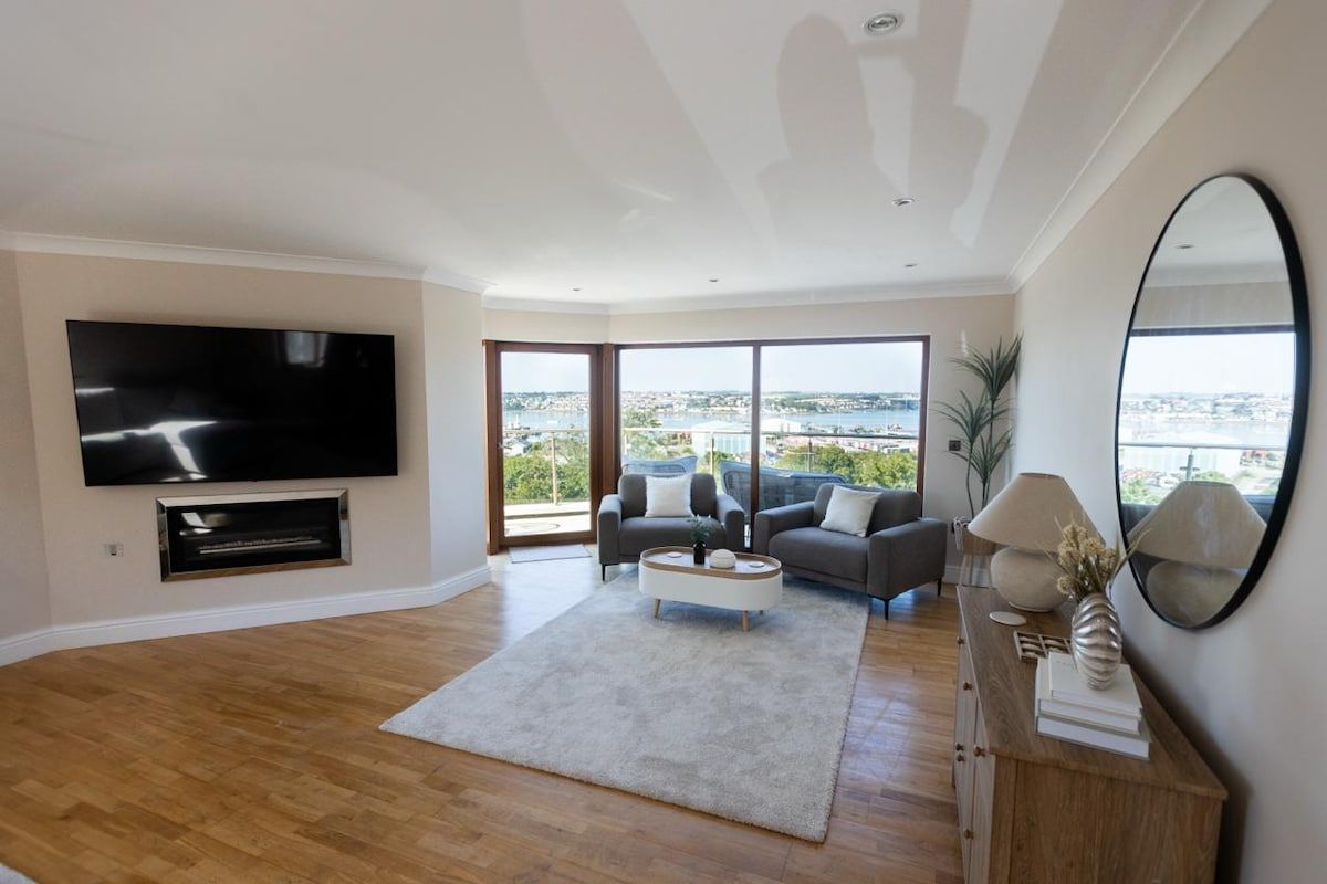 A modern living room with a flat-screen TV, a sofa set, a coffee table, and a large window offering a city view.