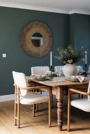 A dining area with a round wooden table, white chairs, and a mirror on the wall. - Preseli Heights Luxury Indoor Pool House with Cinema & Bar (Llanreath)