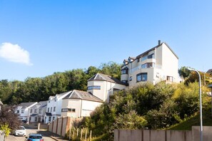 A residential area with houses on a hillside, a clear sky, and a street with parked cars. - Preseli Heights Luxury Indoor Pool House with Cinema & Bar (Llanreath)