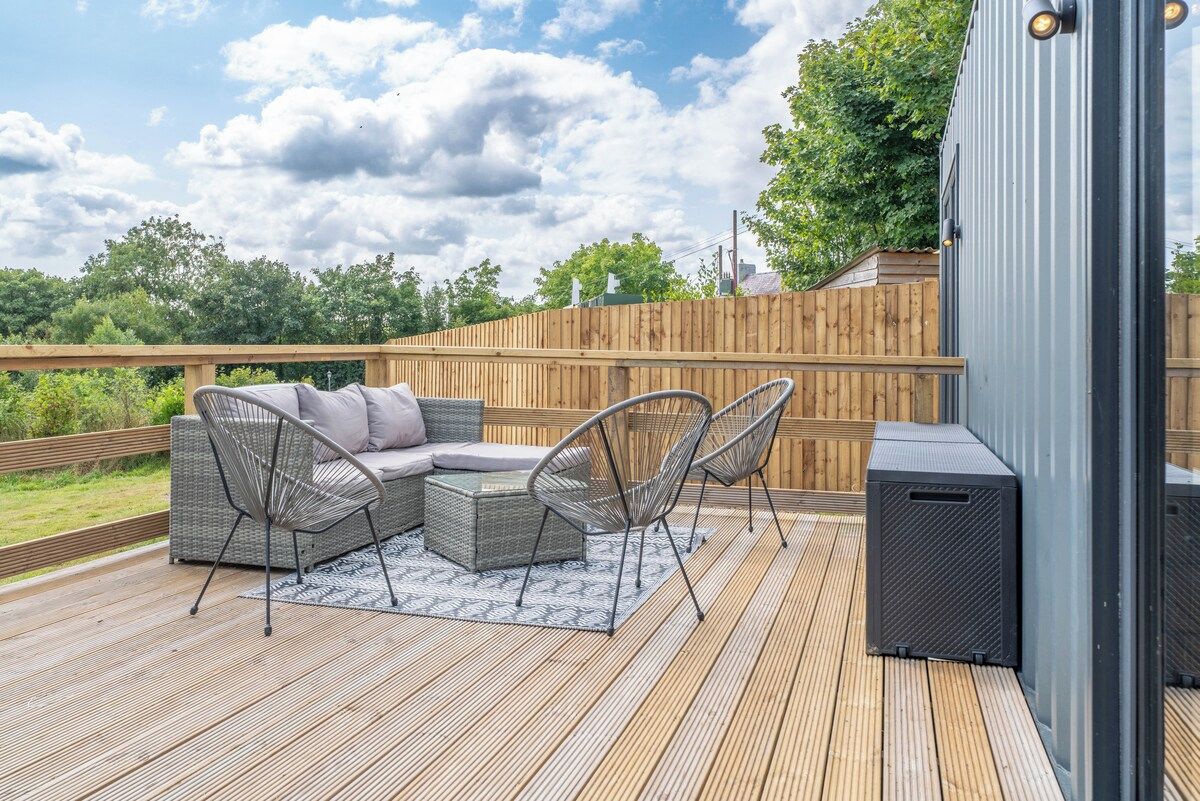 Terraza exterior con sofá y sillones, valla de madera y un altavoz.