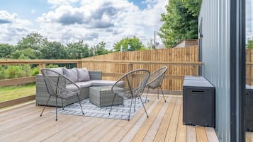 Terraza exterior con sofá y sillones, valla de madera y un altavoz.