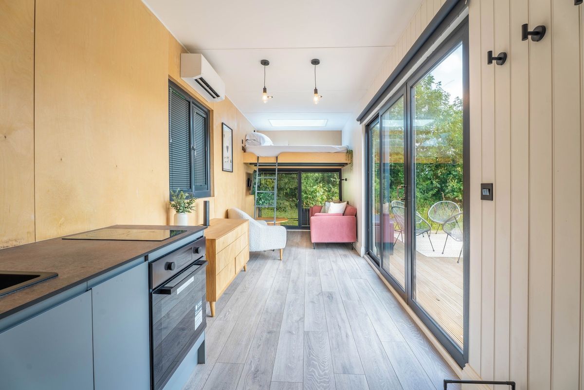 Una cocina moderna con horno empotrado, zona de comedor con sofá rosa y un amplio ventanal corredero que da a un patio exterior.