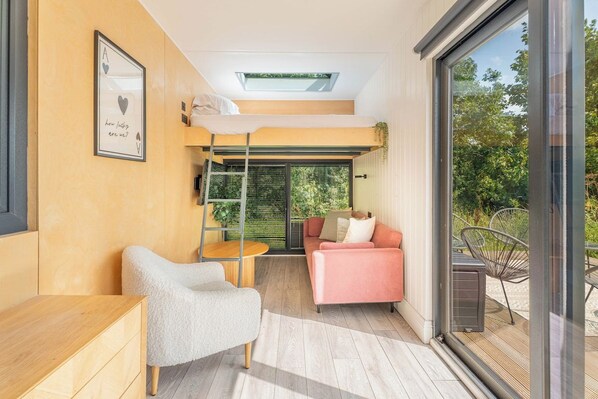 A compact living space with a bunk bed, a small seating area, and a view through a glass door.