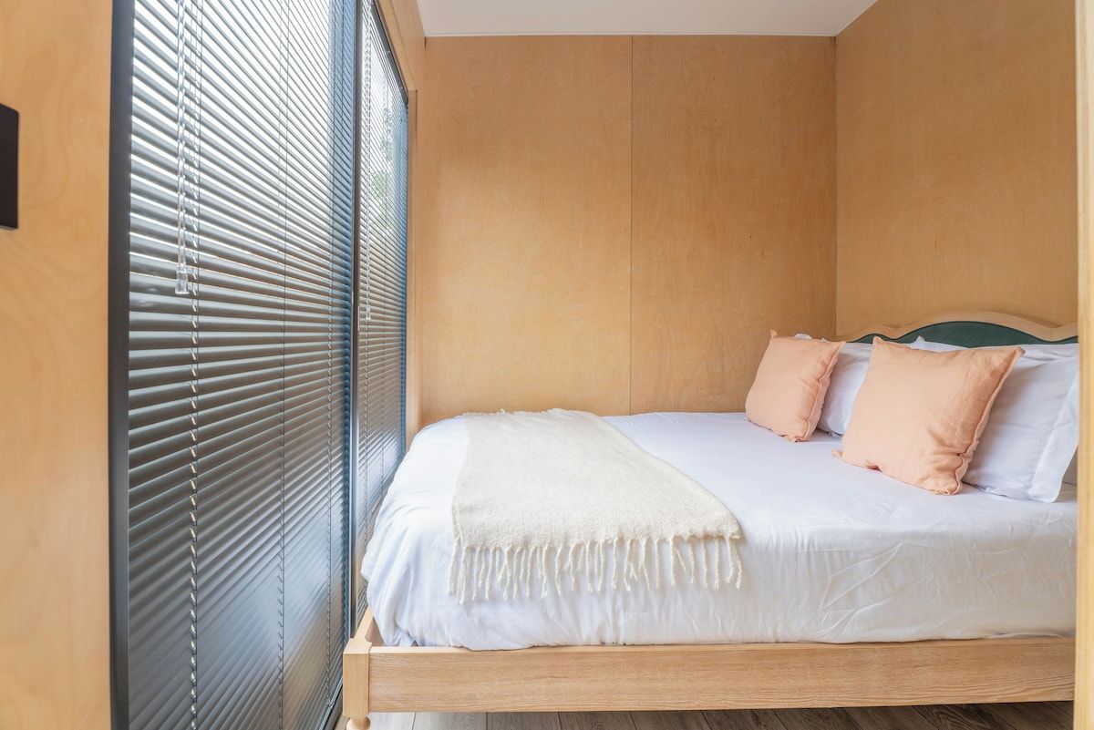 A room with a bed, a window with blinds, and a wooden floor.