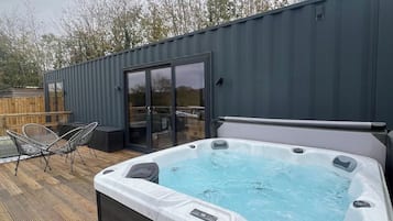 Un bain à remous sur une terrasse en bois, avec une porte vitrée donnant sur un espace de détente extérieur.