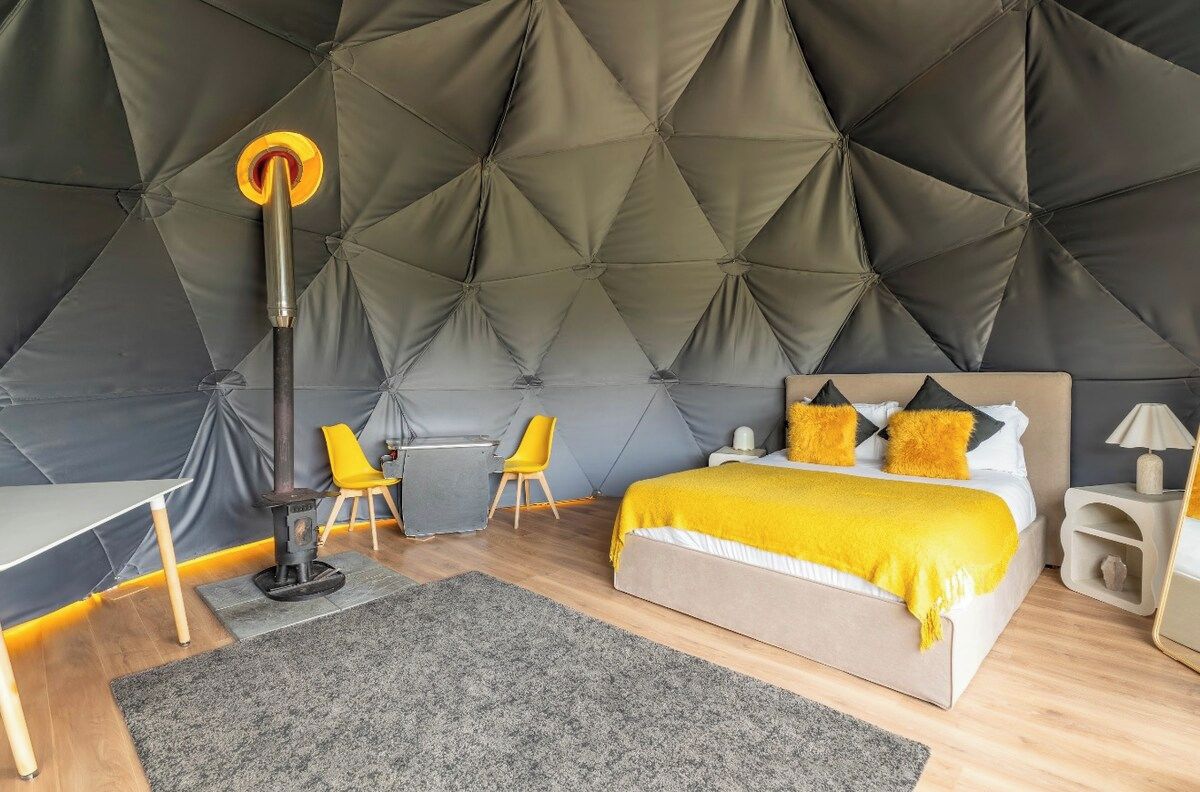 A modern bedroom with a tufted headboard, a bed with a yellow blanket, a desk, a chair, and a floor lamp.