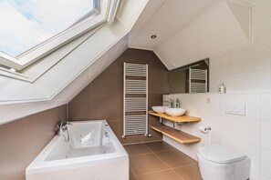 A modern bathroom with a skylight, a freestanding bathtub, a toilet, and a vanity with a mirror. - Charming Villa With Enclosed Garden (De Koog)