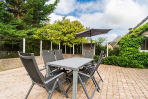 An outdoor patio with a table and chairs, surrounded by greenery and a brick wall. - Charming Villa With Enclosed Garden (De Koog)