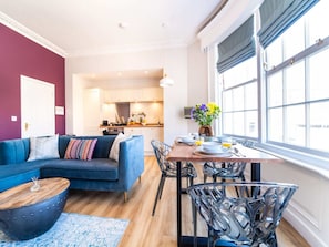 Una sala de estar moderna con un sofá azul, una mesa de comedor con sillas y una cocina al fondo.
