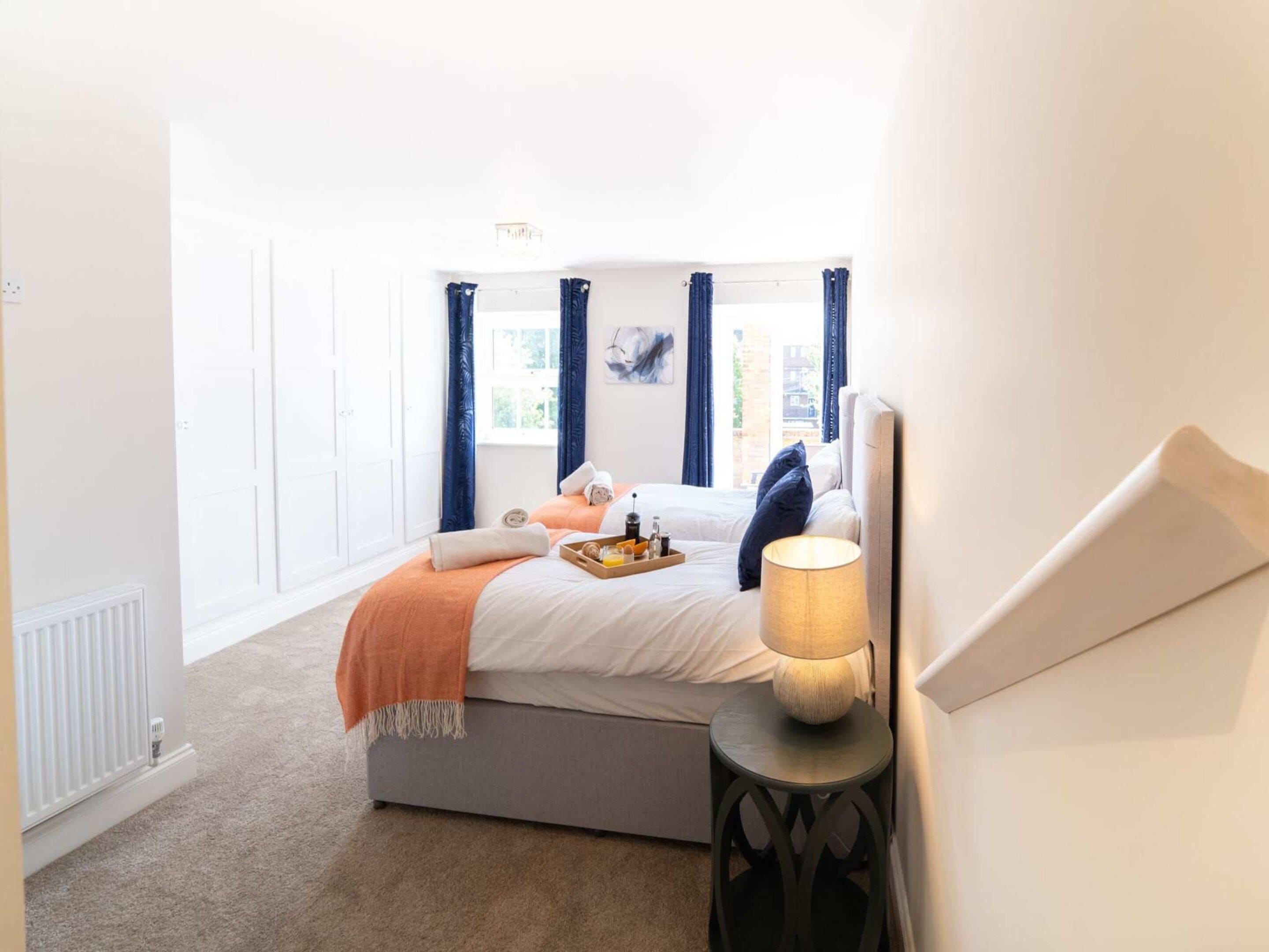 A bedroom with a bed, a bedside table with a lamp, a window with curtains, and a radiator.