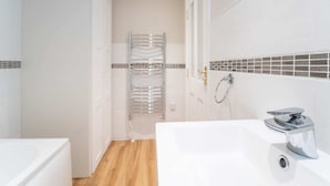 Een badkamer met een witte badkuip, een douchegedeelte en een betegelde muur met een decoratief patroon.
