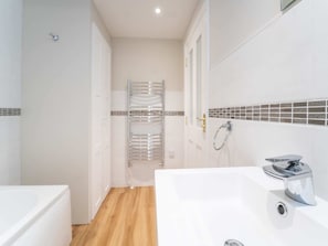 Un baño con una bañera blanca, zona de ducha y pared de azulejos con un diseño decorativo.