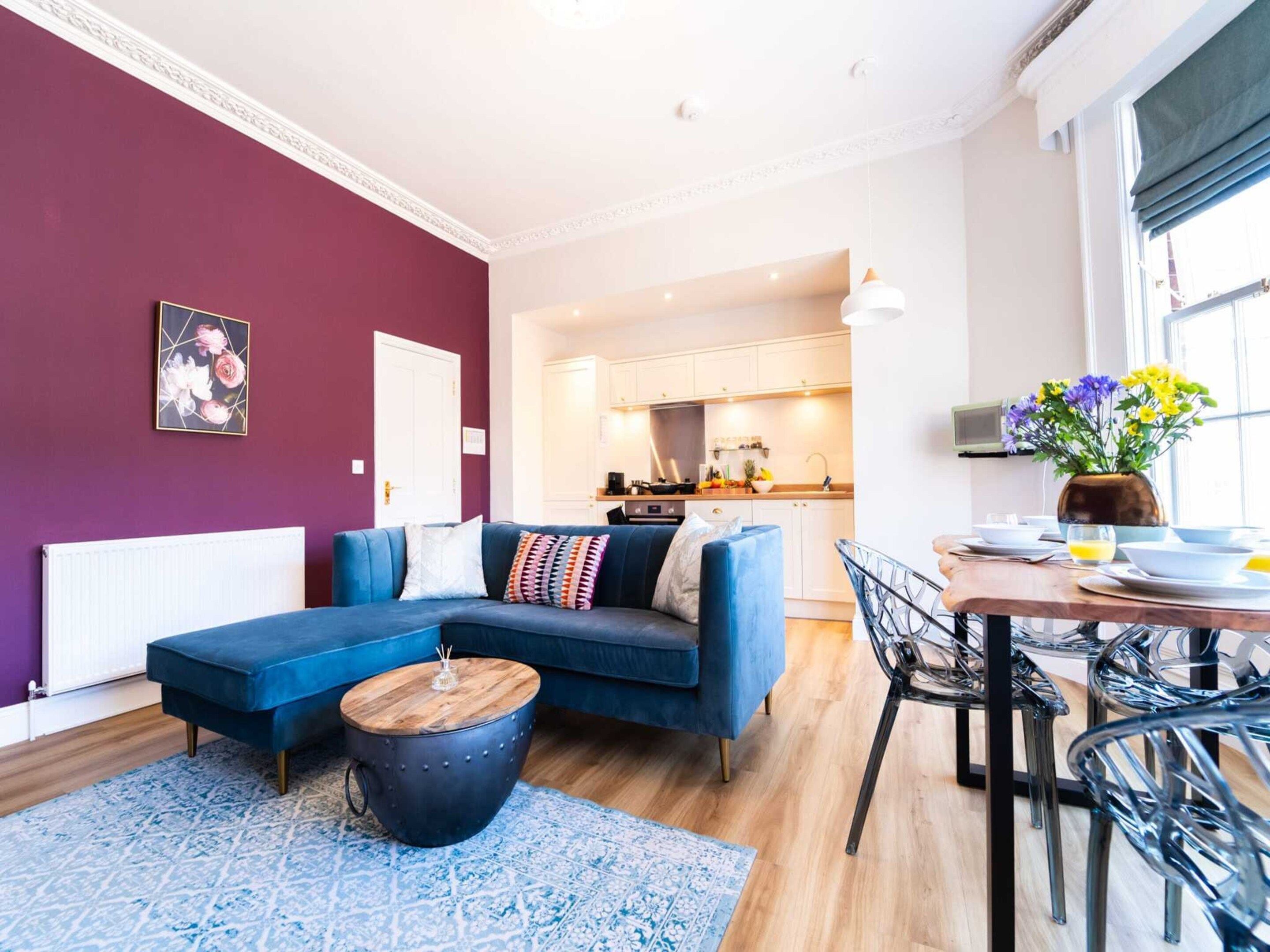 A modern living room with a blue sofa, a round coffee table, and a dining area with chairs and a table.