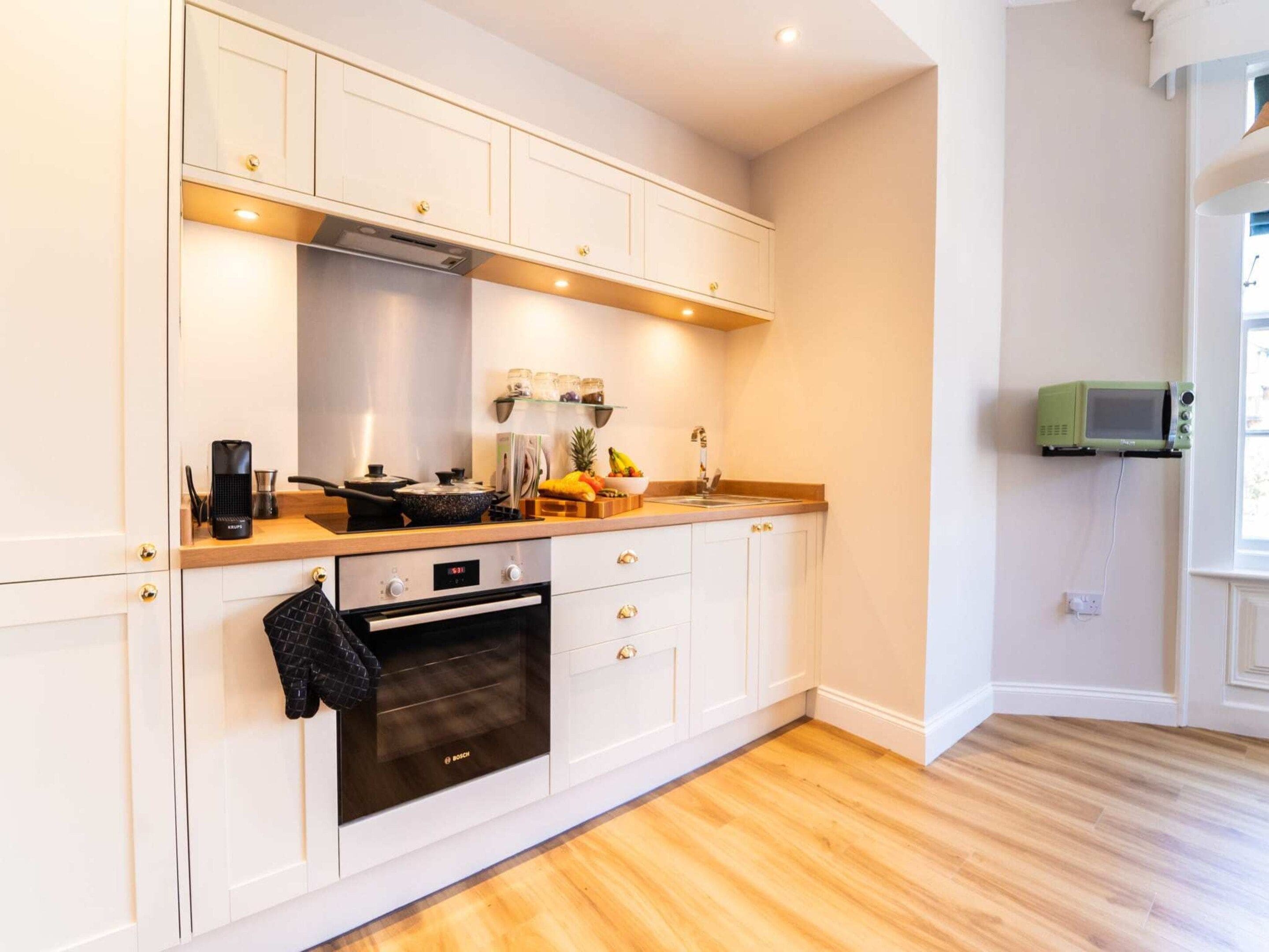 A modern kitchen with white cabinetry, a Bosch oven, a microwave, and a wooden countertop.