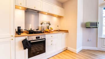 A modern kitchen with white cabinetry, a Bosch oven, a microwave, and a wooden countertop.