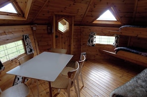 L’intérieur d’une cabine comprenant une table à manger, des chaises, un lit superposé et des fenêtres avec des rideaux.