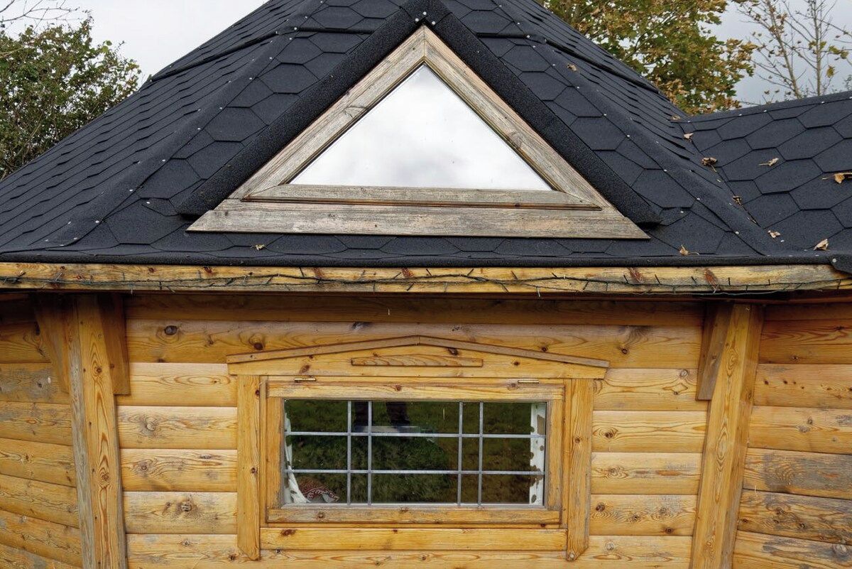 A log cabin with a triangular gable roof and a window with a wooden frame.