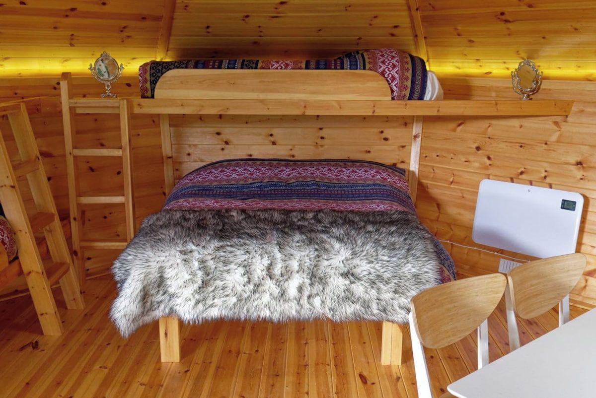 A wooden cabin interior with a bunk bed, a chair, a small table, and a ladder.