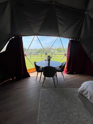 Una carpa con una mesa redonda y sillas, una cama, y vistas a un paisaje verde.
