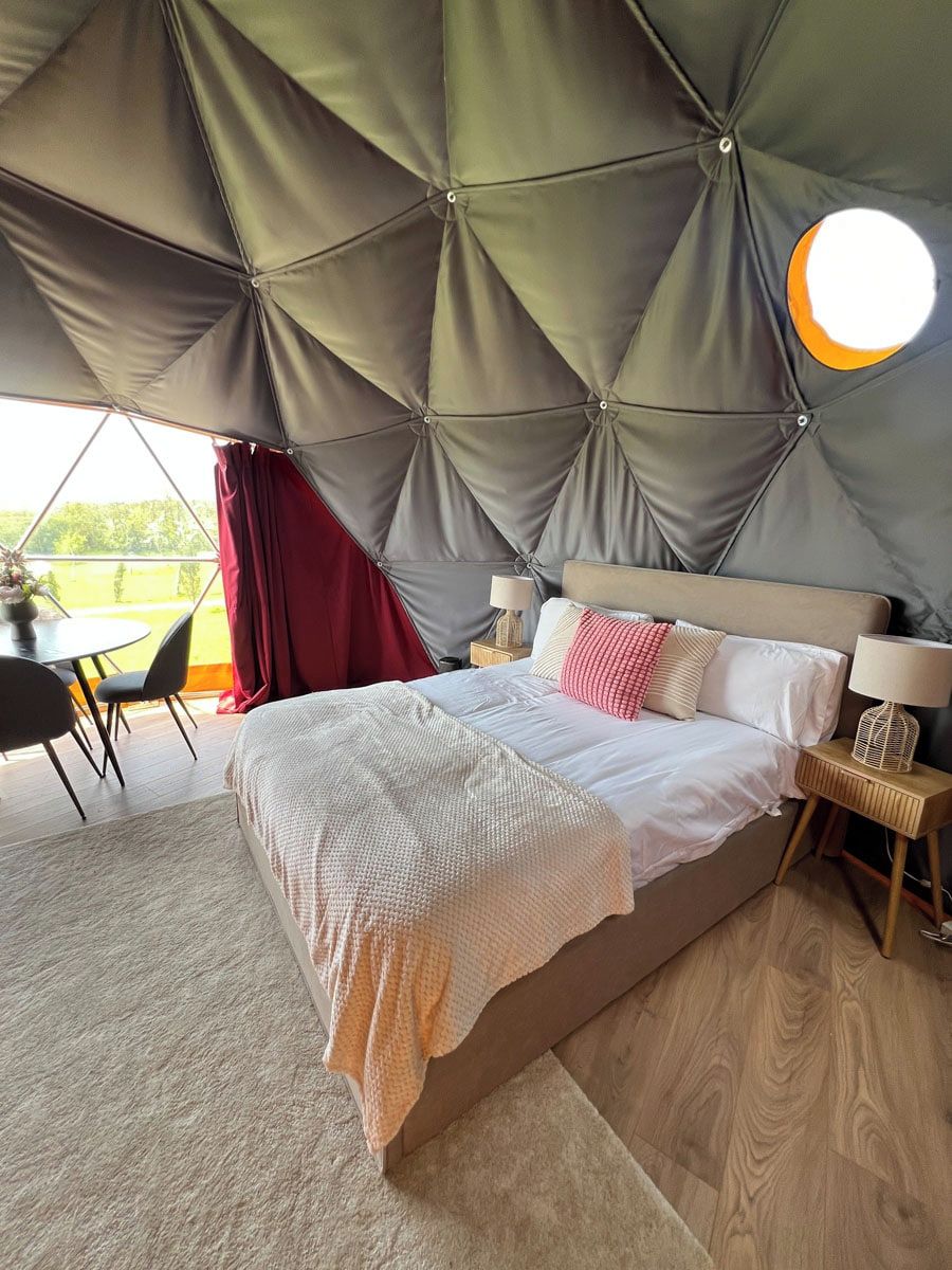 A tent-style bedroom with a bed, bedside tables, and a view of the outdoors.