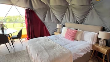A tent-style bedroom with a bed, bedside tables, and a view of the outdoors.