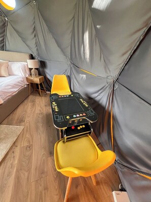 A tent-like room with a bed, a small table with a lamp, and a yellow chair.