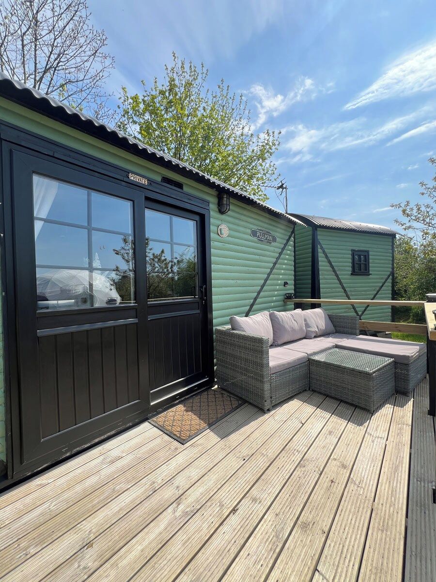 A wooden deck with a wicker sofa and a small table, a black door labeled 'PRIVATE,' and a green building with the name 'PULMAN' on the side.