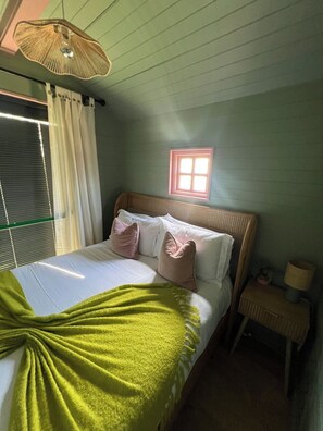 A bedroom with a bed, pillows, a bedside table, a lamp, a window, and a ceiling fan.