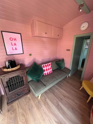 Ein Zimmer mit rosafarbenen Wänden, einem grünen Sofa, einem Holzschrank und einem gelben Sessel.