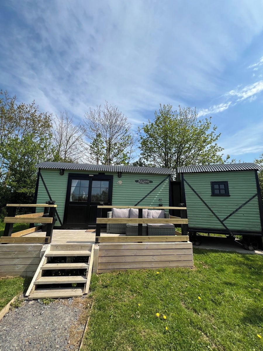 Une petite cabane verte, de plain-pied, avec une porte et des fenêtres, un petit porche avec des marches et une enseigne sur laquelle on peut lire « FULLMAN ».