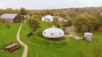 A rural setting with a large geodesic dome structure surrounded by a well-maintained lawn, a wooden barn, and a small shed.