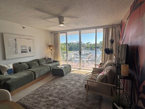 Ett modernt vardagsrum med en grön soffa, ett soffbord och utsikt över en småbåtshamn genom stora glasdörrar.