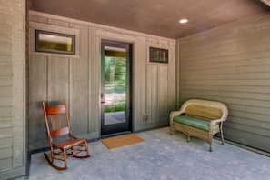A covered porch with a rocking chair and a wicker bench.