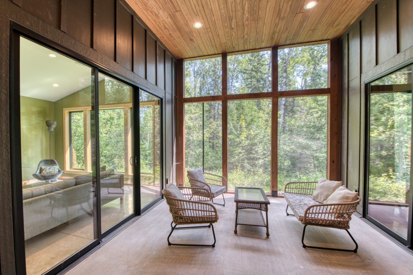 A modern interior with large windows, wicker furniture, and a wooden ceiling.