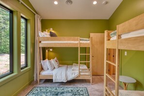 Une chambre avec un lit superposé, une fenêtre, une petite table et un tapis à motifs.